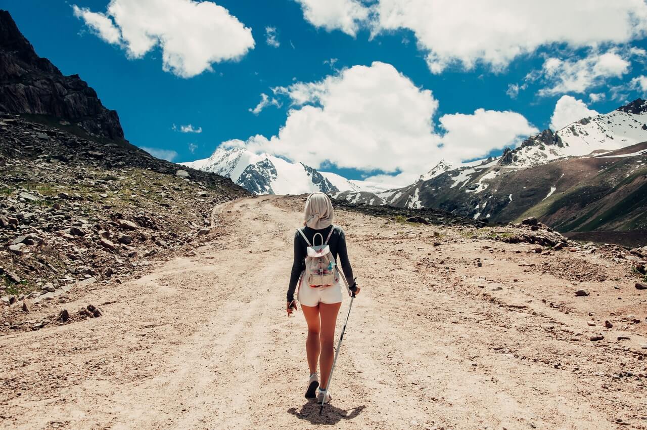 Woman hiking an upward path, surrounded by mountains on three sides, under a brilliant blue sky.