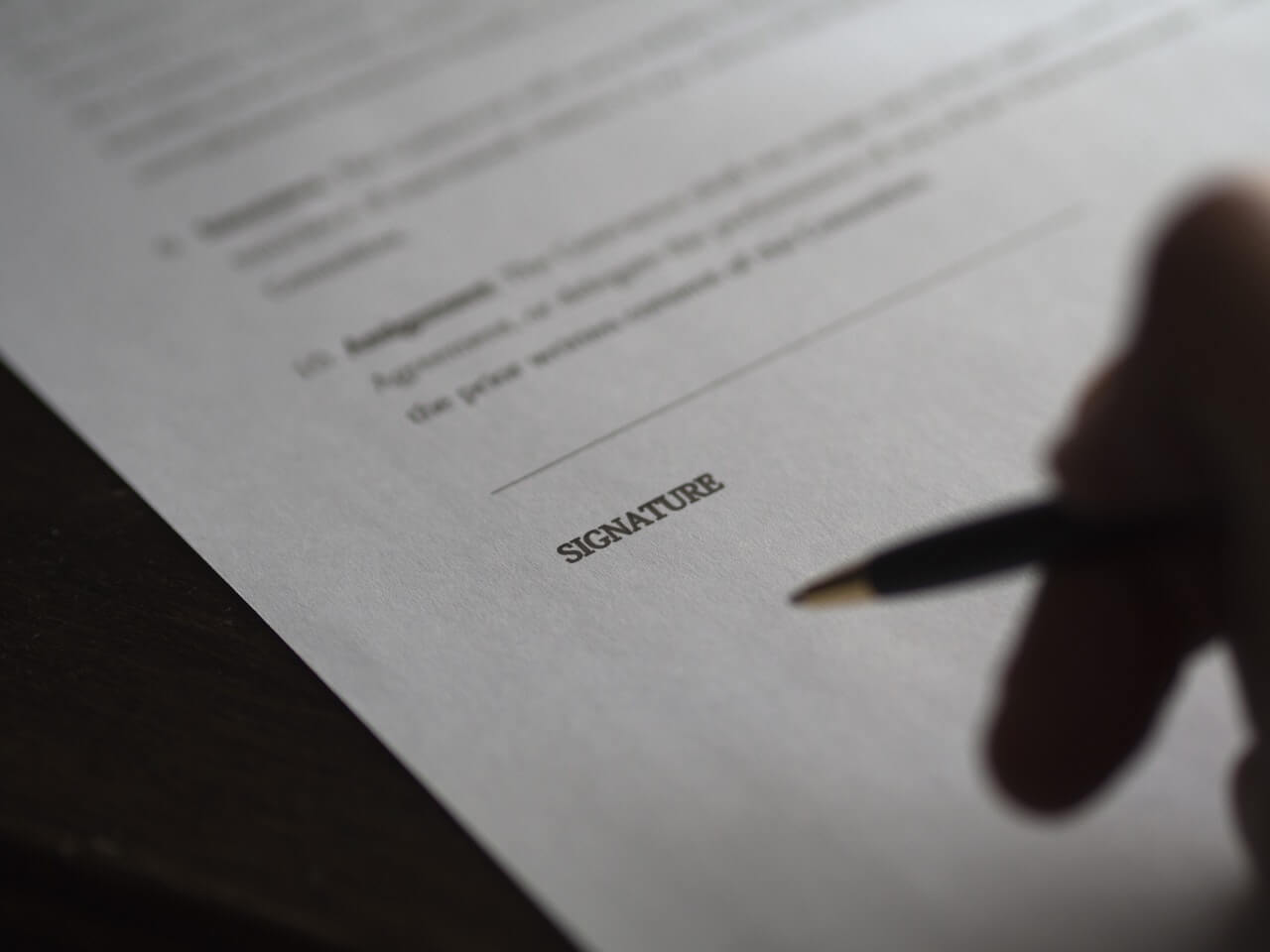 A silhoutted hand holding a pen, hovering above a contract.