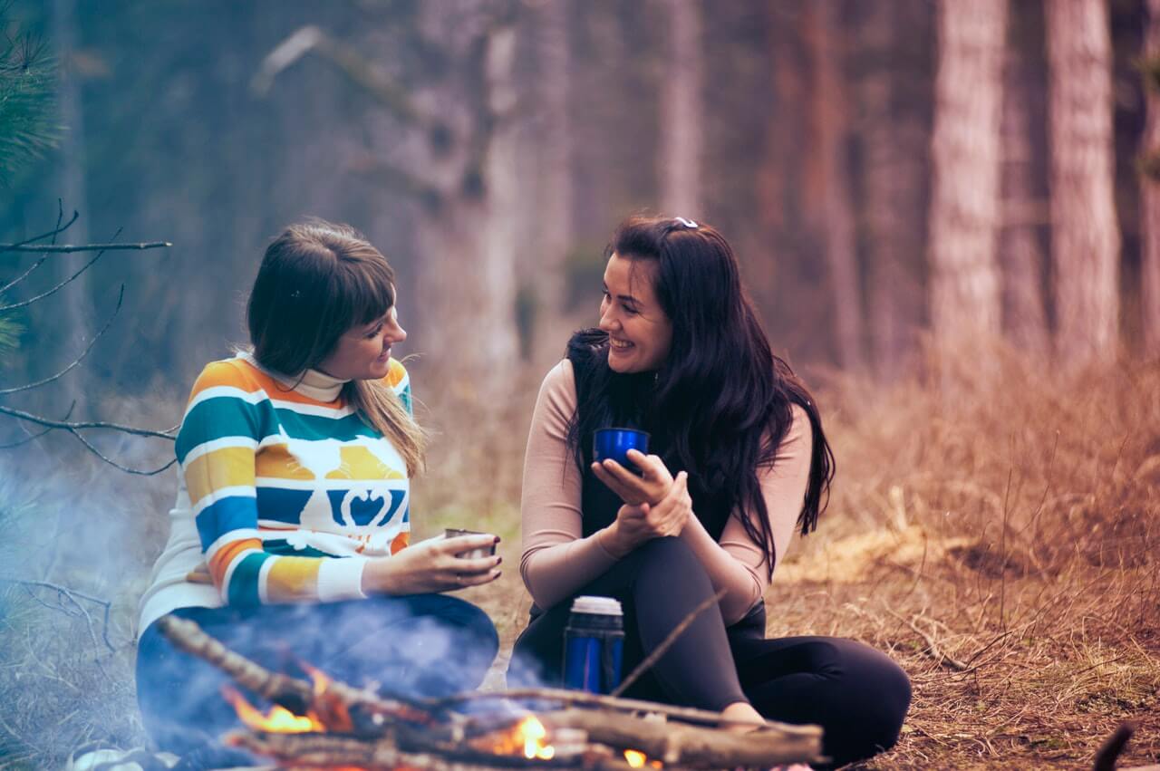 Two friends sharing a warm drink around the campfire.